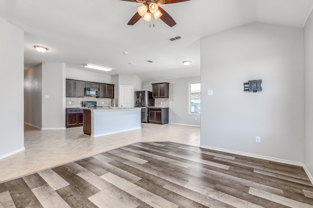 kitchen featuring black appliances, light wood-type flooring, an island with sink, dark brown cabinetry, and vaulted ceiling