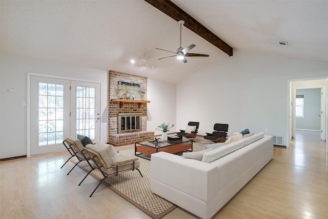 living room with ceiling fan, a textured ceiling, light wood-type flooring, a fireplace, and lofted ceiling with beams