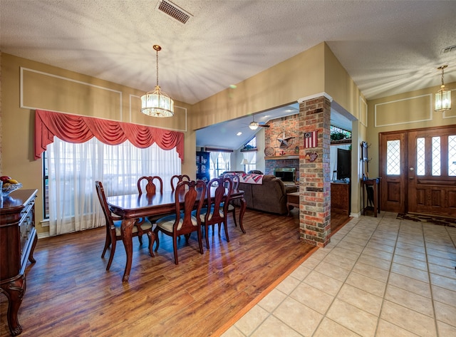 dining room with hardwood / wood-style floors, ceiling fan with notable chandelier, a textured ceiling, and a brick fireplace