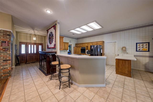 kitchen featuring black appliances, a kitchen breakfast bar, crown molding, a textured ceiling, and kitchen peninsula