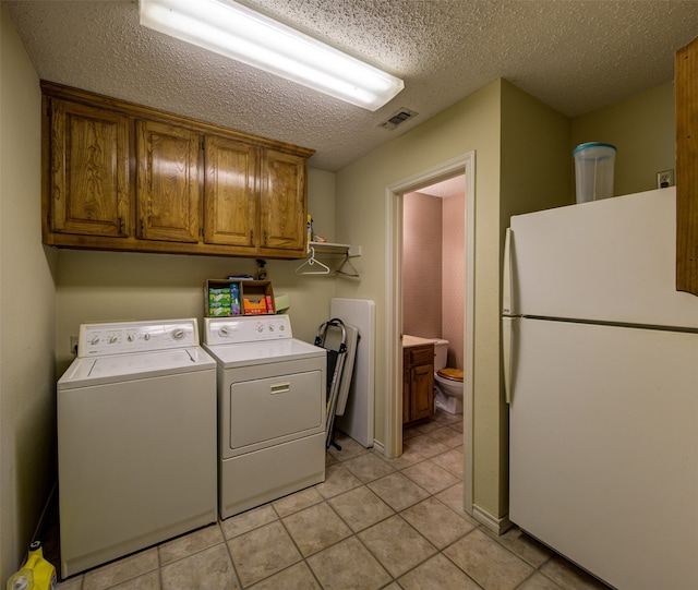 laundry area featuring washing machine and dryer, light tile patterned floors, cabinets, and a textured ceiling