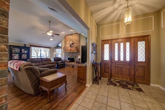 entrance foyer featuring lofted ceiling, ceiling fan, a textured ceiling, a fireplace, and light tile patterned flooring