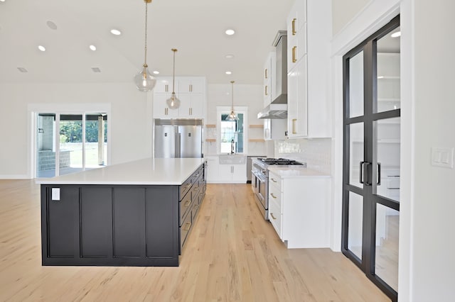 kitchen with a spacious island, hanging light fixtures, high end appliances, white cabinets, and light hardwood / wood-style floors