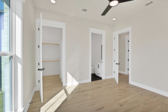 unfurnished bedroom with connected bathroom, a closet, a walk in closet, light wood-type flooring, and ceiling fan