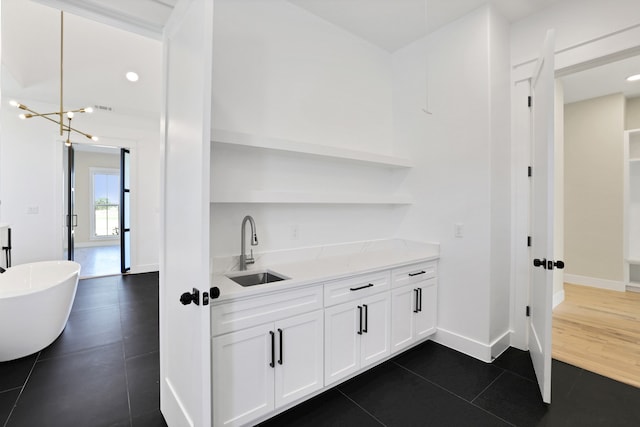 bar with light stone counters, white cabinetry, dark tile patterned floors, a notable chandelier, and sink