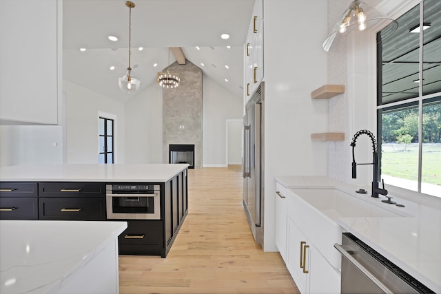 kitchen featuring appliances with stainless steel finishes, white cabinetry, light wood-type flooring, beamed ceiling, and decorative light fixtures