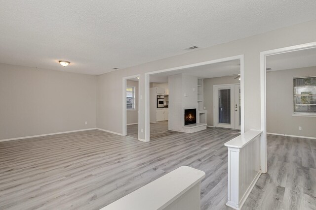 509 Ridgeview Dr, Rockwall, TX 75087 - unfurnished living room featuring a textured ceiling, light wood finished floors, baseboards, a lit fireplace, and ceiling fan