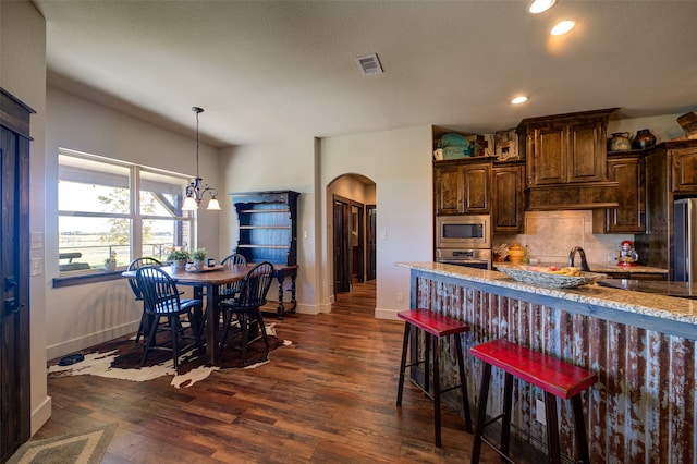 kitchen featuring dark wood-type flooring, light stone countertops, a notable chandelier, a kitchen bar, and stainless steel appliances