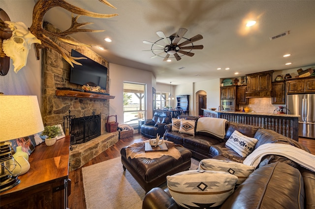 living room with hardwood / wood-style floors, ceiling fan, and a stone fireplace