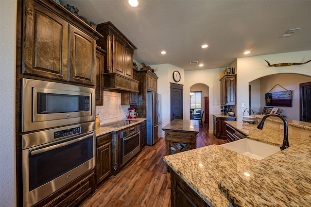 kitchen featuring appliances with stainless steel finishes, dark hardwood / wood-style flooring, dark brown cabinets, sink, and a center island with sink