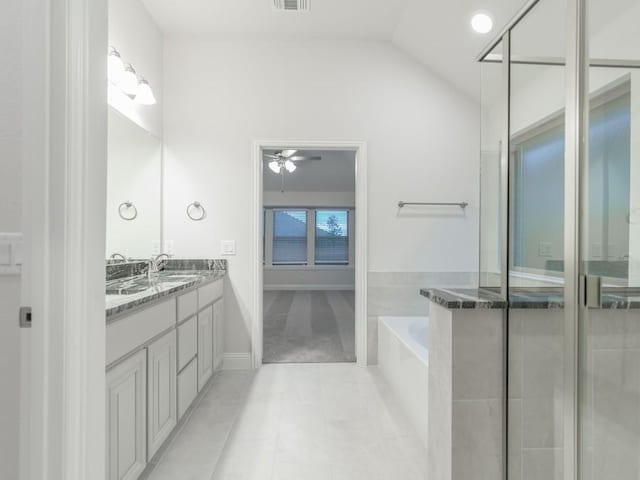 bathroom with lofted ceiling, vanity, tile patterned flooring, and tiled tub