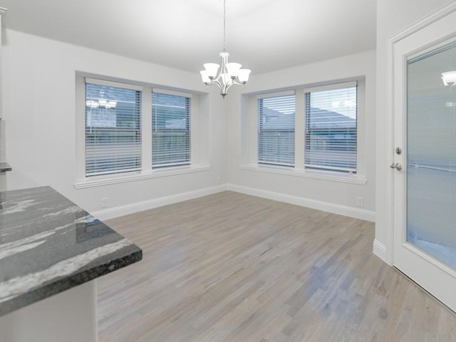 unfurnished dining area featuring lofted ceiling, a notable chandelier, and light hardwood / wood-style floors