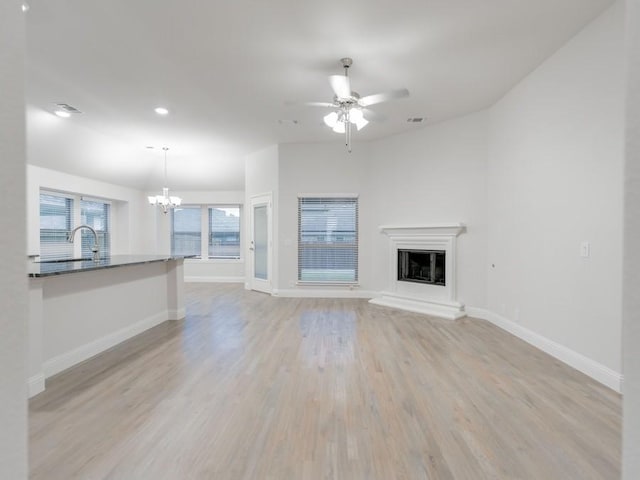 unfurnished living room with ceiling fan with notable chandelier, sink, and light wood-type flooring