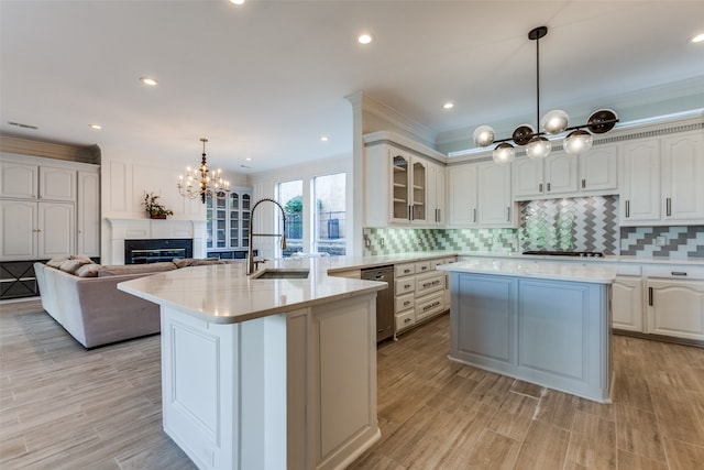 kitchen with ornamental molding, sink, an island with sink, and decorative light fixtures