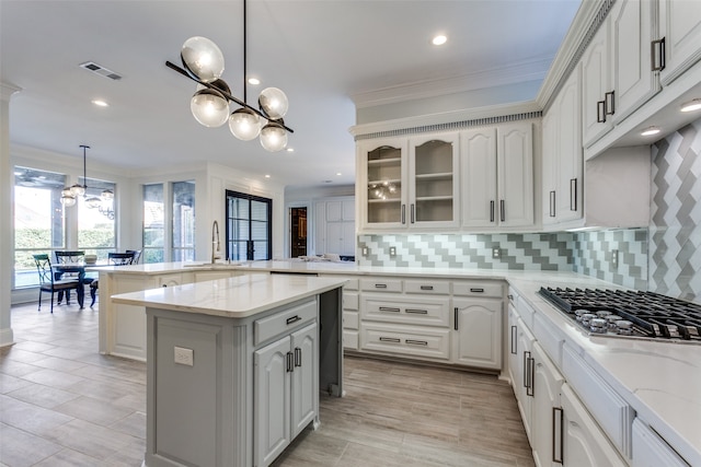 kitchen featuring a kitchen island, stainless steel gas cooktop, white cabinetry, decorative light fixtures, and crown molding