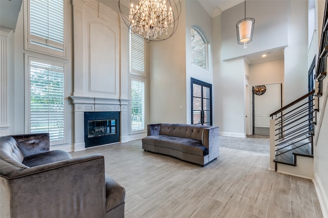 living room with an inviting chandelier, ornamental molding, a high ceiling, and light hardwood / wood-style floors