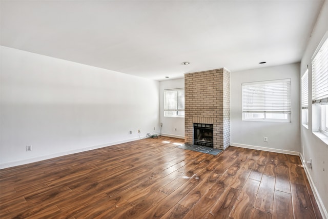 unfurnished living room featuring dark hardwood / wood-style flooring and a brick fireplace