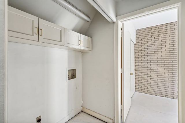 laundry area featuring brick wall, hookup for a washing machine, and cabinets