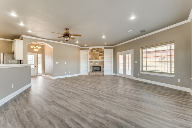 unfurnished living room featuring light hardwood / wood-style floors, crown molding, a stone fireplace, and ceiling fan