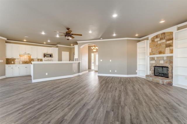 unfurnished living room featuring a fireplace, ornamental molding, built in shelves, light hardwood / wood-style floors, and ceiling fan