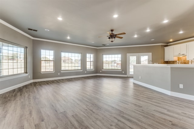 unfurnished living room with light hardwood / wood-style floors, crown molding, and a wealth of natural light