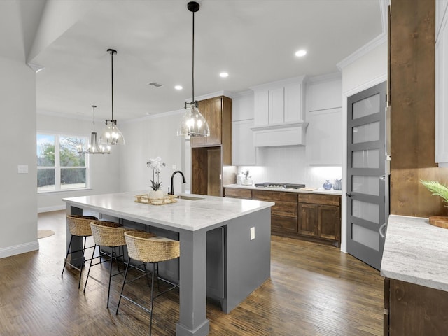 kitchen with sink, white cabinetry, hanging light fixtures, a large island, and light stone countertops