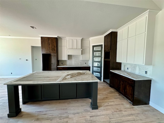 kitchen with a large island, light hardwood / wood-style flooring, dark brown cabinetry, and backsplash