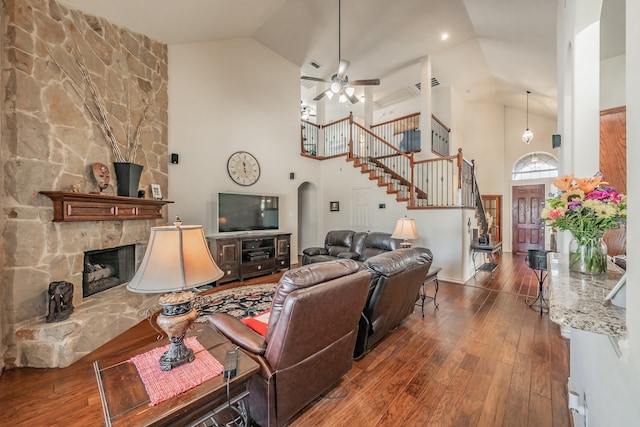 living room with dark wood-type flooring, ceiling fan, high vaulted ceiling, and a stone fireplace