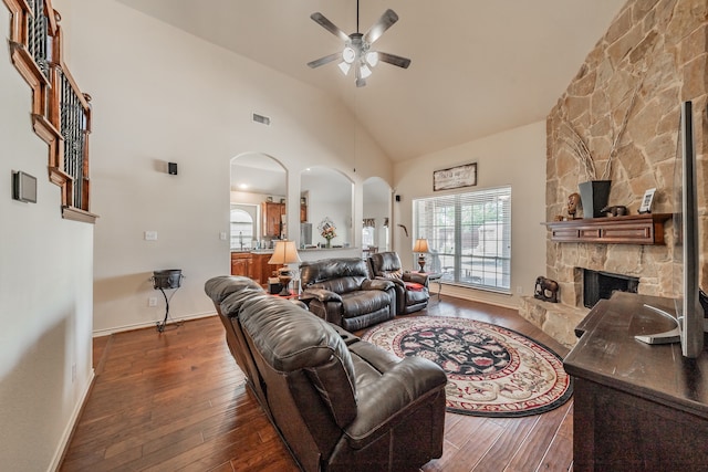 living room featuring ceiling fan, high vaulted ceiling, dark hardwood / wood-style floors, and a stone fireplace