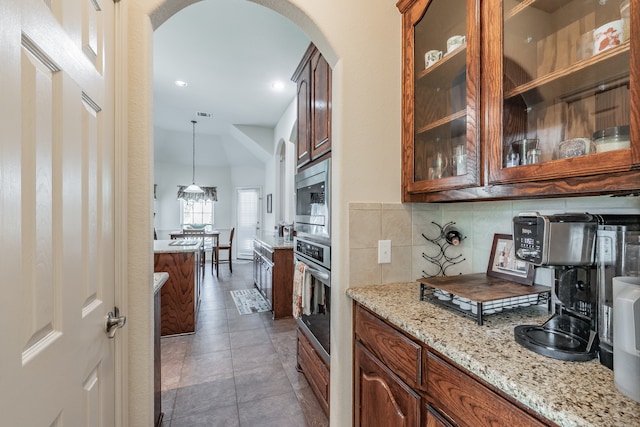 kitchen featuring decorative backsplash, dark tile patterned flooring, hanging light fixtures, appliances with stainless steel finishes, and light stone counters