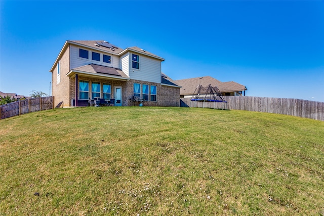 rear view of property with a trampoline and a lawn