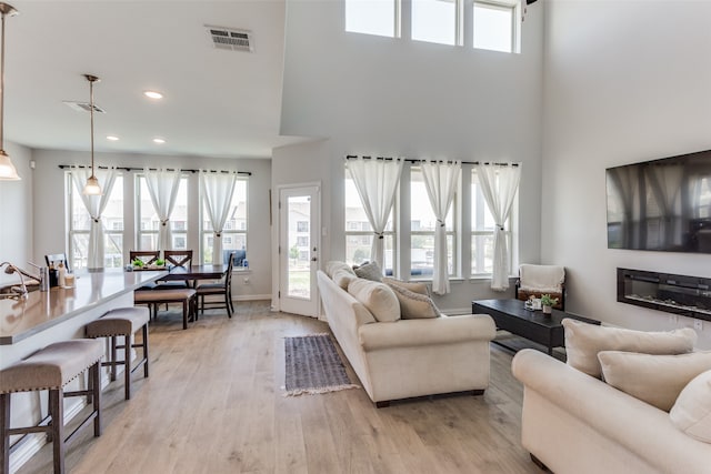 living room with sink, a towering ceiling, a wealth of natural light, and light wood-type flooring