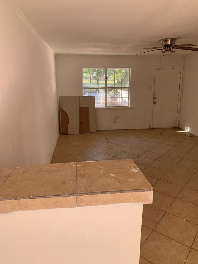 empty room with crown molding, light tile patterned flooring, and ceiling fan