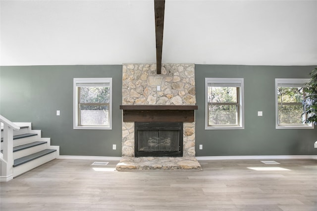 unfurnished living room featuring beam ceiling, a stone fireplace, and light wood-type flooring