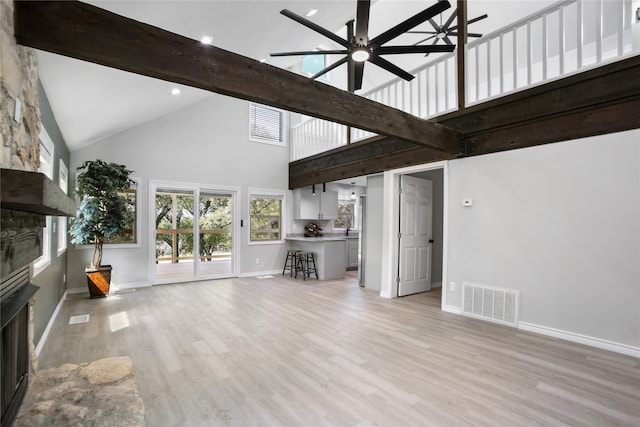 unfurnished living room with high vaulted ceiling, beamed ceiling, a fireplace, light hardwood / wood-style floors, and ceiling fan