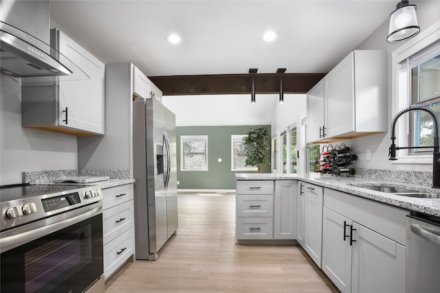 kitchen with a healthy amount of sunlight, stainless steel appliances, wall chimney exhaust hood, and white cabinets