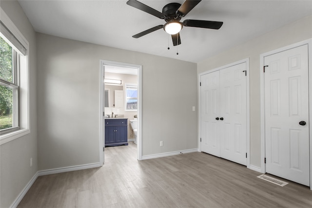 unfurnished bedroom featuring connected bathroom, ceiling fan, multiple closets, and light hardwood / wood-style flooring