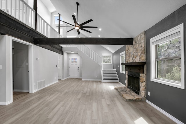 unfurnished living room with a stone fireplace, beamed ceiling, light hardwood / wood-style flooring, high vaulted ceiling, and ceiling fan