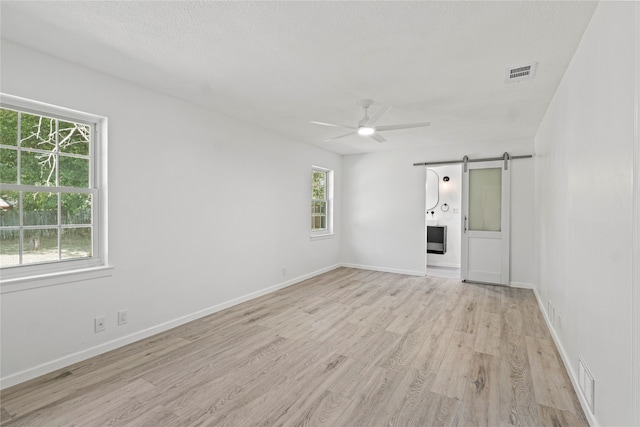 unfurnished room featuring a barn door, a healthy amount of sunlight, ceiling fan, and light hardwood / wood-style floors