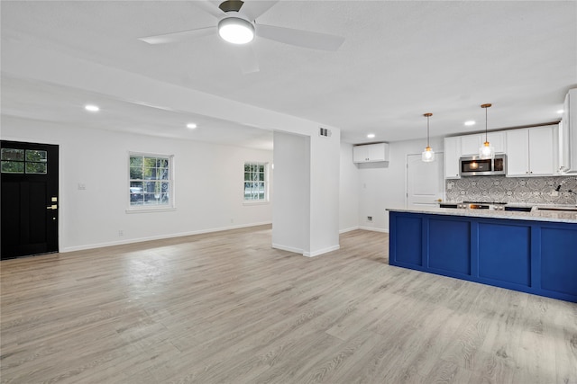 kitchen with ceiling fan, white cabinetry, hanging light fixtures, backsplash, and light wood-type flooring