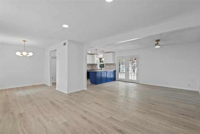 unfurnished living room featuring ceiling fan with notable chandelier, french doors, and light hardwood / wood-style flooring