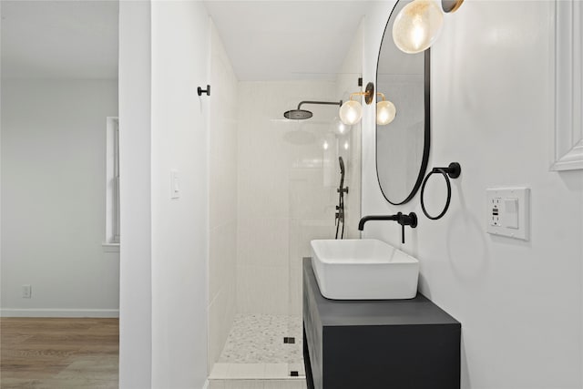 bathroom with a tile shower, vanity, and wood-type flooring