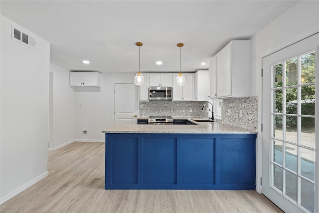 kitchen with light hardwood / wood-style flooring, backsplash, pendant lighting, white cabinets, and appliances with stainless steel finishes