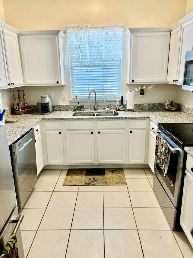 kitchen with light tile patterned floors, appliances with stainless steel finishes, white cabinetry, light stone countertops, and sink