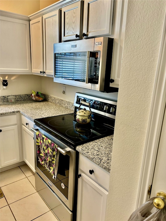 kitchen with appliances with stainless steel finishes, light stone counters, white cabinets, and light tile patterned floors