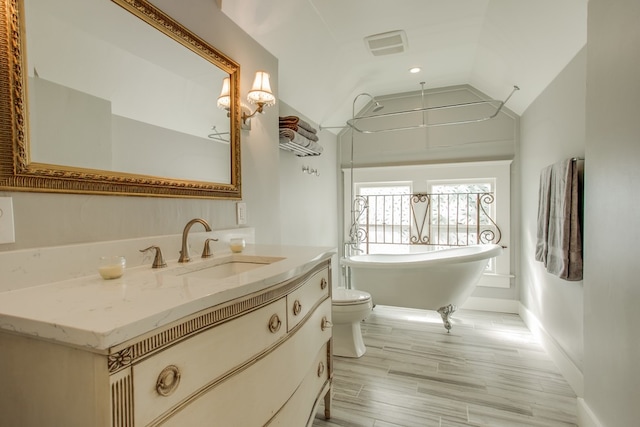 bathroom with toilet, hardwood / wood-style floors, vaulted ceiling, a bathing tub, and vanity