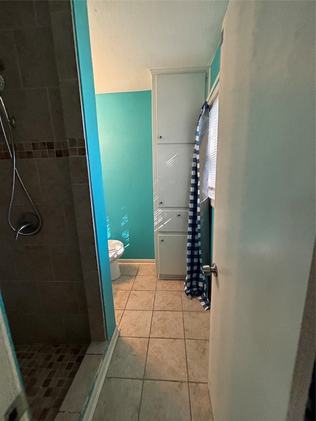 bathroom with tile patterned floors, a tile shower, and toilet