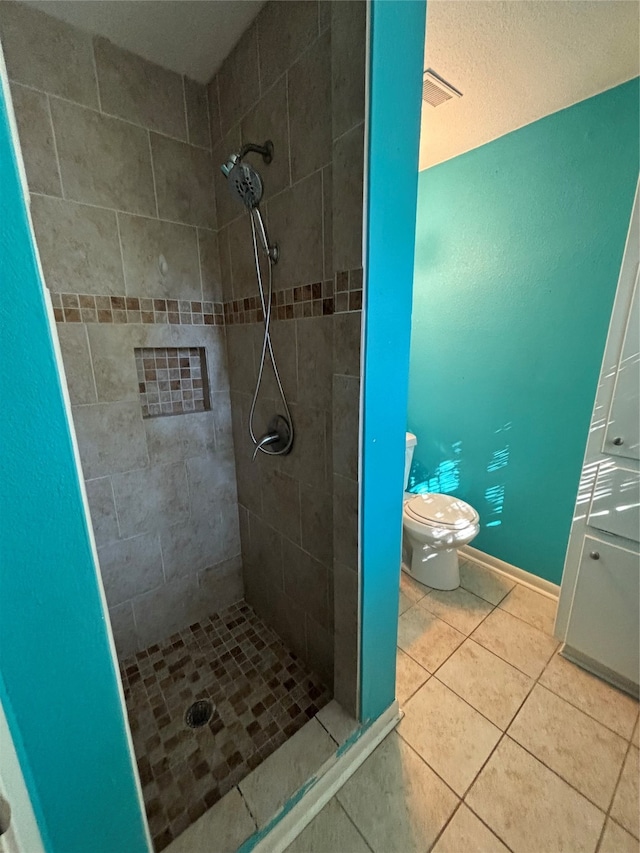 bathroom featuring a tile shower, toilet, and tile patterned flooring