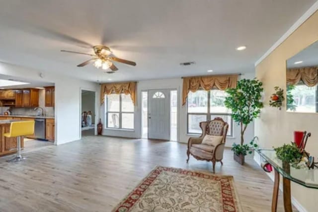 living room featuring light wood-type flooring, ceiling fan, crown molding, and sink