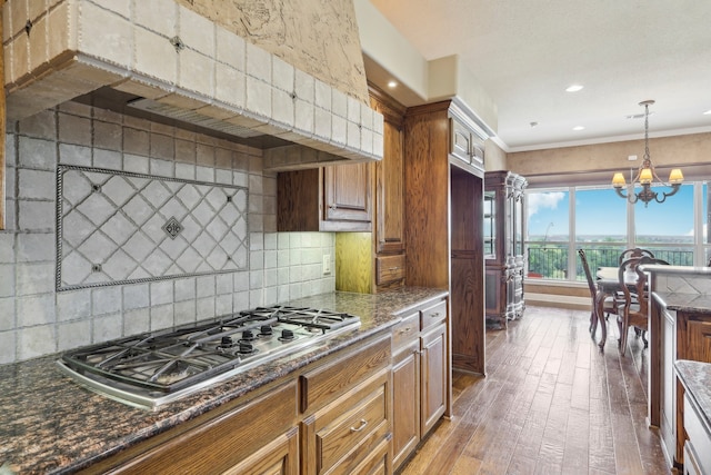 kitchen featuring backsplash, dark hardwood / wood-style floors, dark stone countertops, ornamental molding, and stainless steel gas cooktop